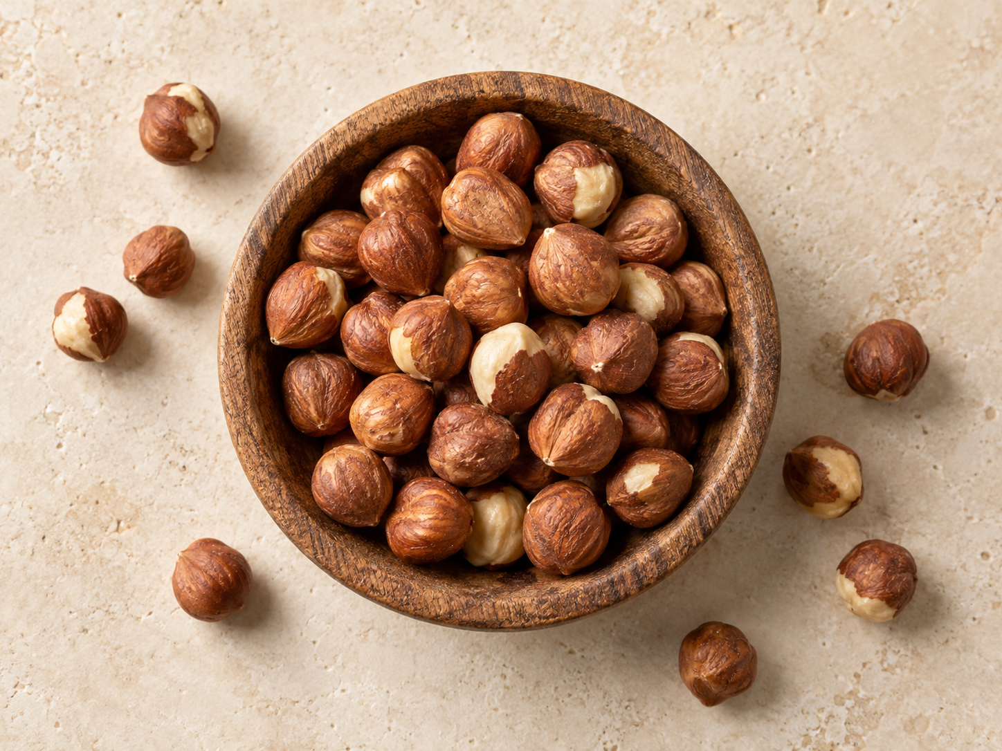 Shelled hazelnut kernels with natural brown skin in a wooden bowl, viewed from above