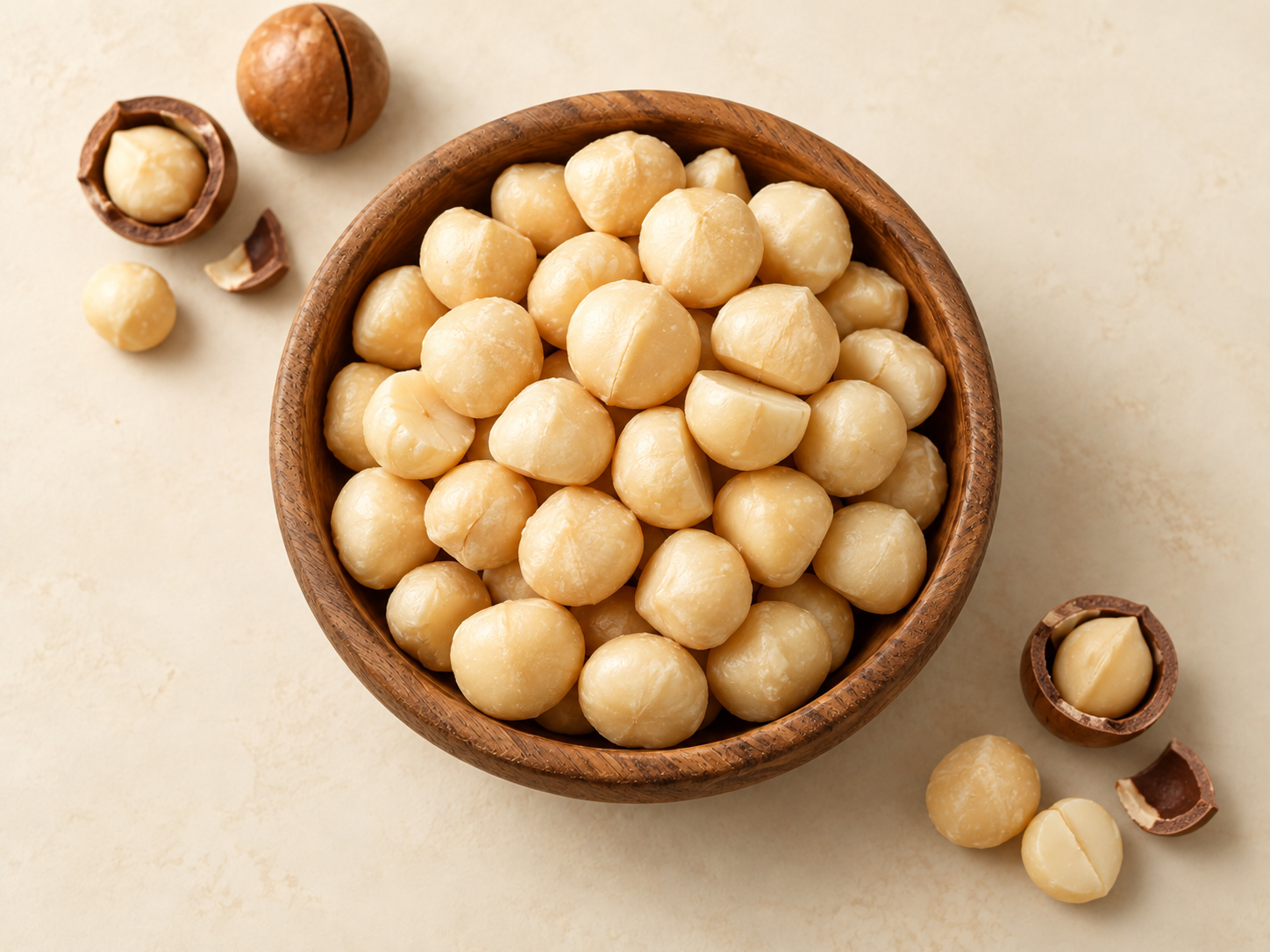 Macadamia kernels in a wooden bowl with in-shell macadamias alongside, viewed from above